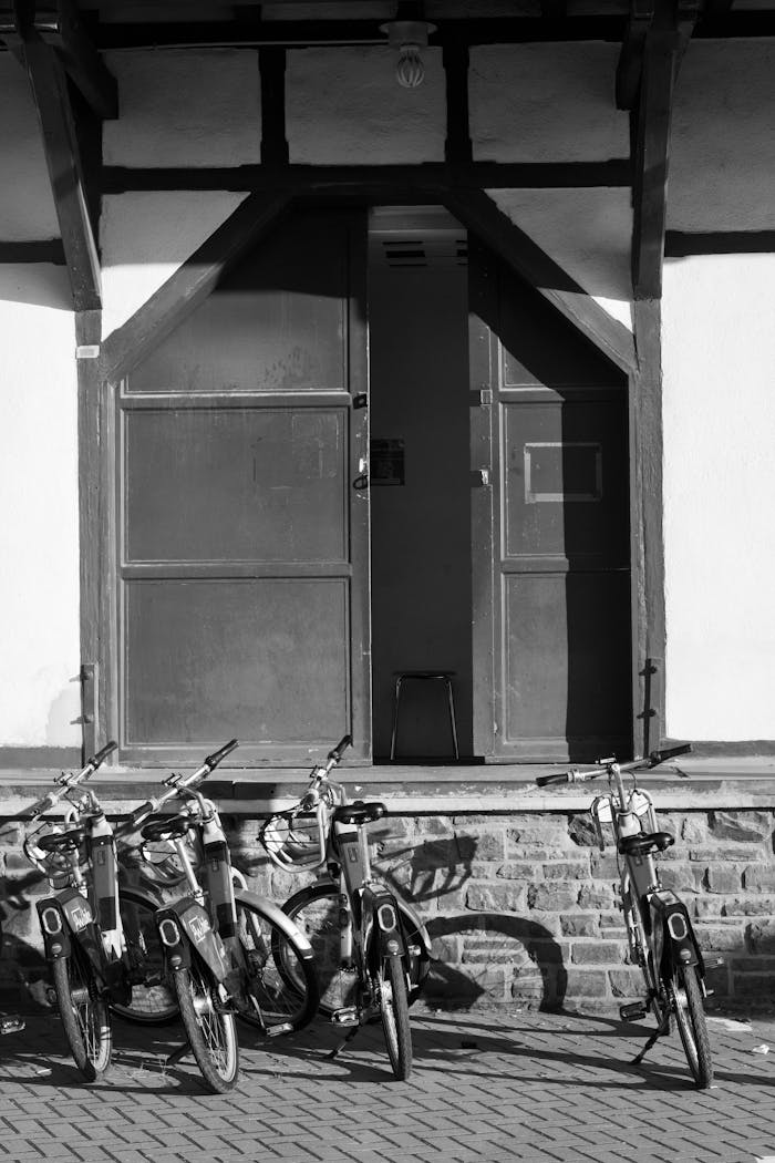 Black and white photo of vintage bicycles against a rustic building facade, exuding nostalgic charm.
